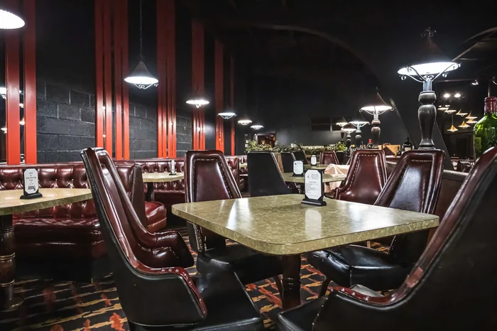The dining room of Johnny’s Café: deep buttoned leather chairs around set tables, dark ceiling and warm lamps.